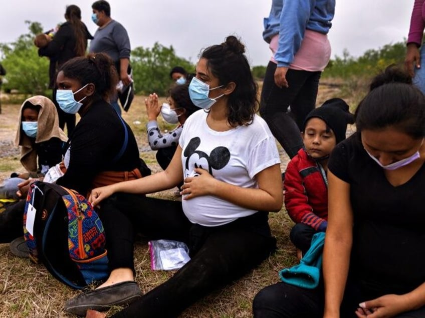 LA JOYA, TEXAS - APRIL 13: Pregnant women sit with their families while waiting to board a U.S. Customs and Border Protection bus to an immigrant processing center after crossing the border from Mexico on April 13, 2021 in La Joya, Texas. A surge of immigrants making the arduous journey …