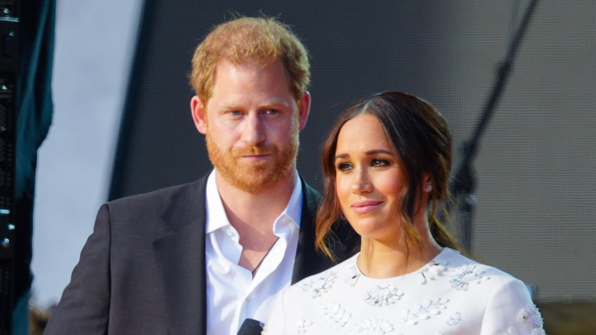 A close-up of Meghan Markle and Prince Harry looking disappointed on stage.