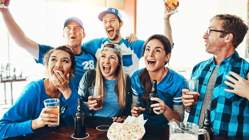 Football fans celebrate while drinking beer with popcorn at the table.