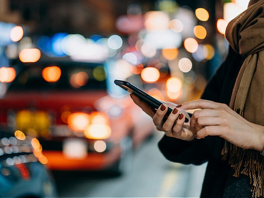 Close up of young woman using mobile app device on smartphone to arrange taxi ride in down