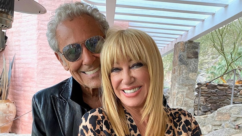 Alan Hamel wearing a leather jacket and smiling holding Suzanne Somers wearing a leopard blouse.