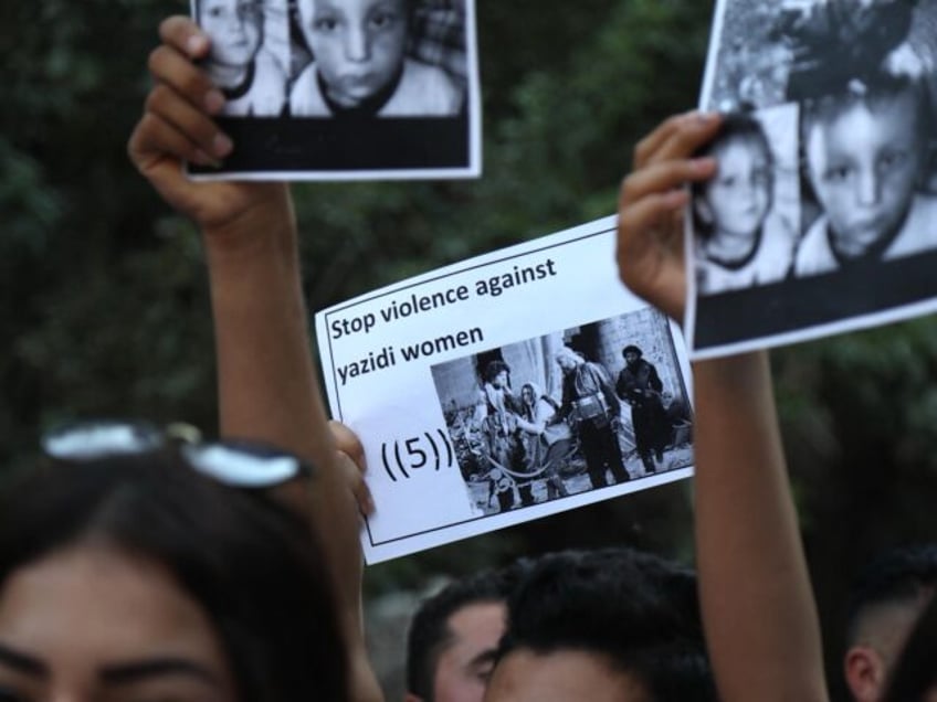 Iraqi Yezidi women raise placards with pictures of vicitms of the 2014 invasion of their r