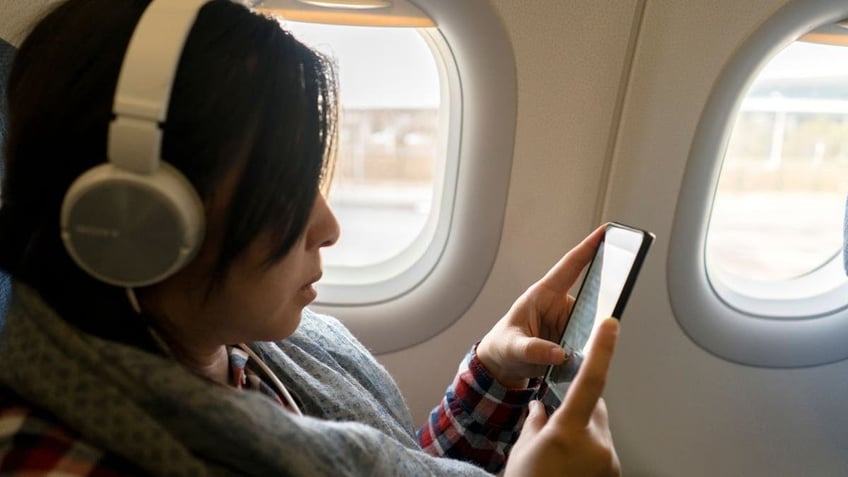 A woman talks on a phone aboard a plane.