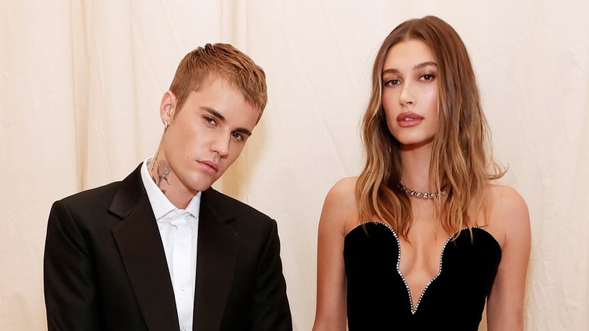 Justin Bieber in a black suit poses next to wife Hailey Bieber in a black plunging dress on the carpet