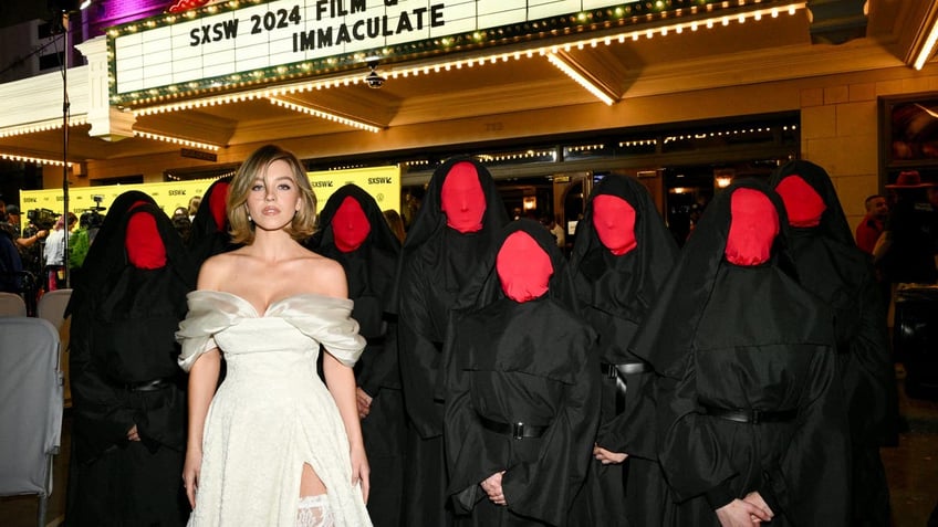 sydney sweeney posing with people dressed as nuns with their faces covered in red masks at the SXSW premiere of immaculate