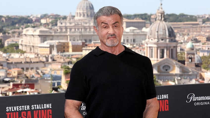 Sylvester Stallone in a black t-shirt with the backdrop of Rome behind him