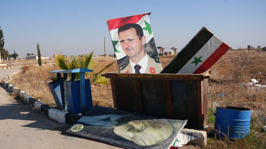 TOPSHOT - A picture taken at the entrance of the Kweyris military airfield in the eastern part of Aleppo province on December 3, 2024 shows a portrait of  Syria's President Bashar al-Assad and a national flag in the garbage dumpster following the take over of the area by rebel groups. A war monitor on December 1 said Ankara-backed groups seized control of the towns of Safireh and Khanasser southeast of Aleppo from government forces, and also took the Kweyris military airport.