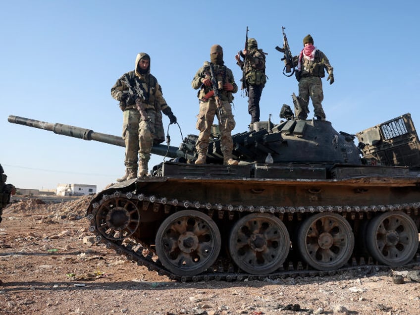 Syrian opposition fighters stand atop a seized military armored vehicle on the outskirts o