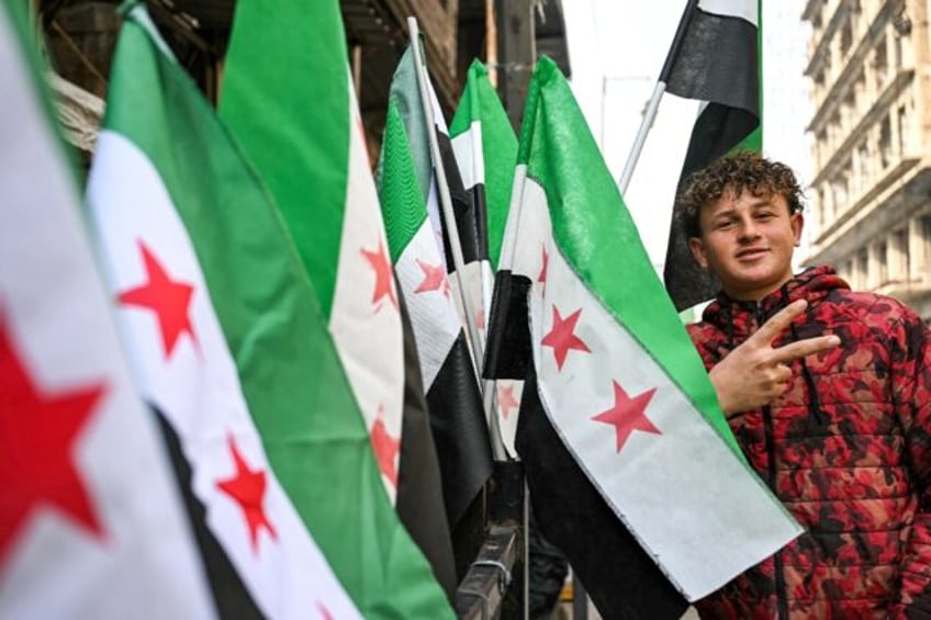 A man poses next to Syrian independence-era flags for sale at a stall in Aleppo city