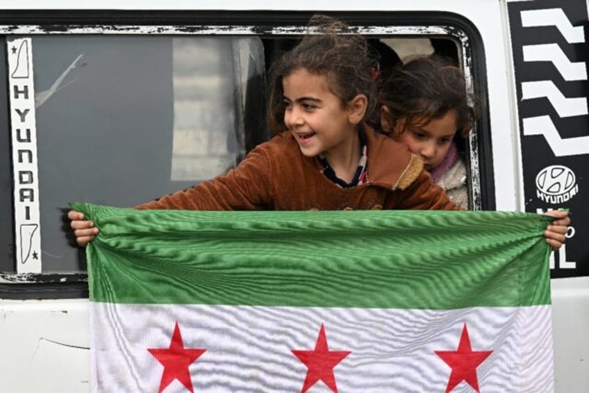 A girl holds an independence-era Syrian flag out of the window of a bus at the entrance to