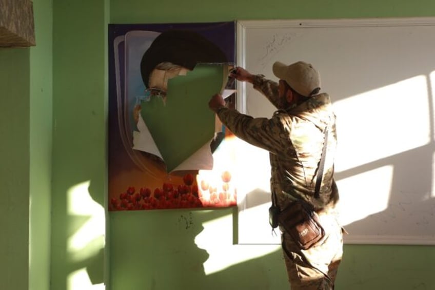 A fighter rips a portrait of slain Hezbollah leader Hassan Nasrallah, in a building in Qus