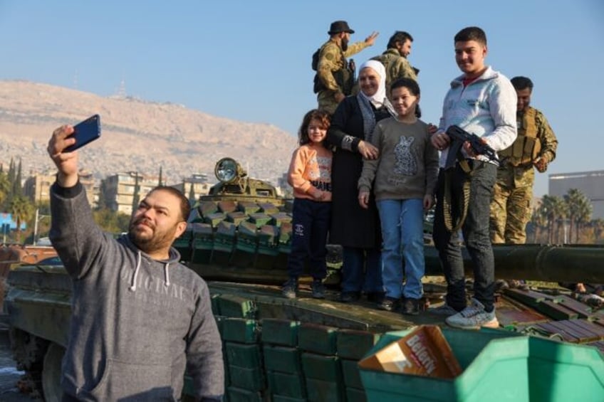 A man takes a selfie with his family standing atop a tank as they celebrate in Damascus on