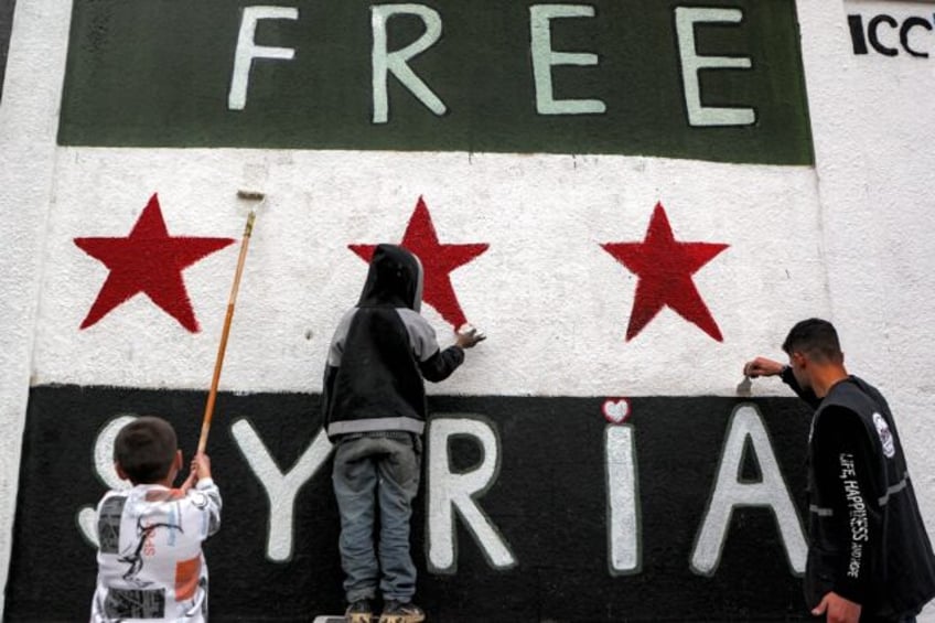 Syrians paint a mural of independence-era flag on a wall in the old city of Homs