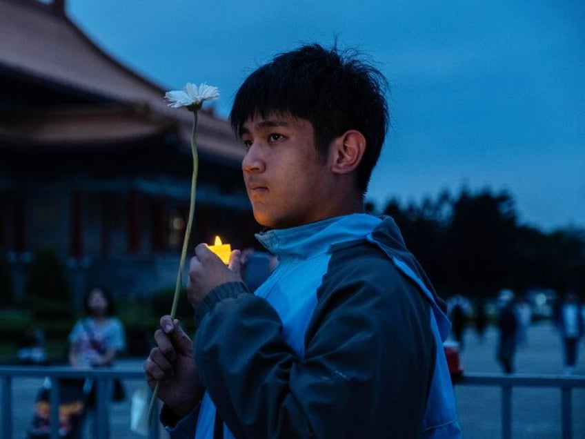 An attendee holds an electric candle and a flower during a vigil at the Liberty Square of