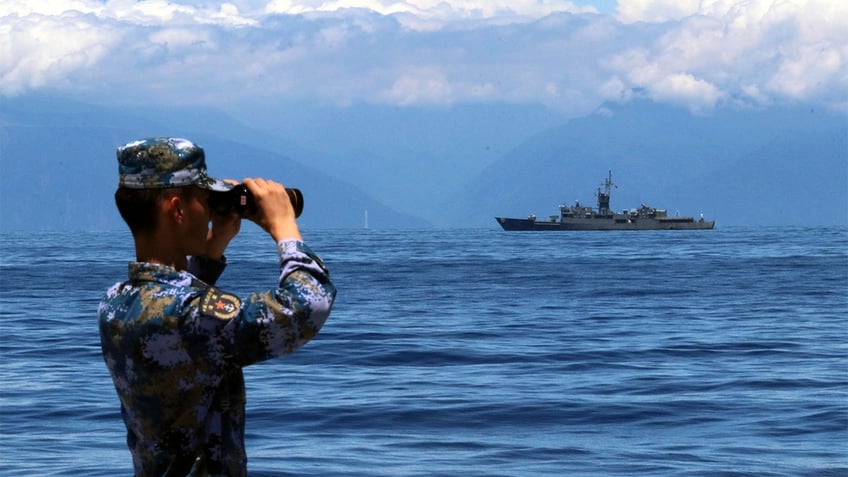 Chinese soldier looking through binoculars with a military ship in the background