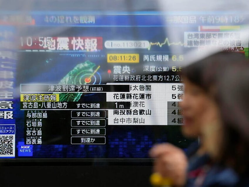 People walk along a sidewalk by a TV showing a breaking news on tsunami for Okinawa region