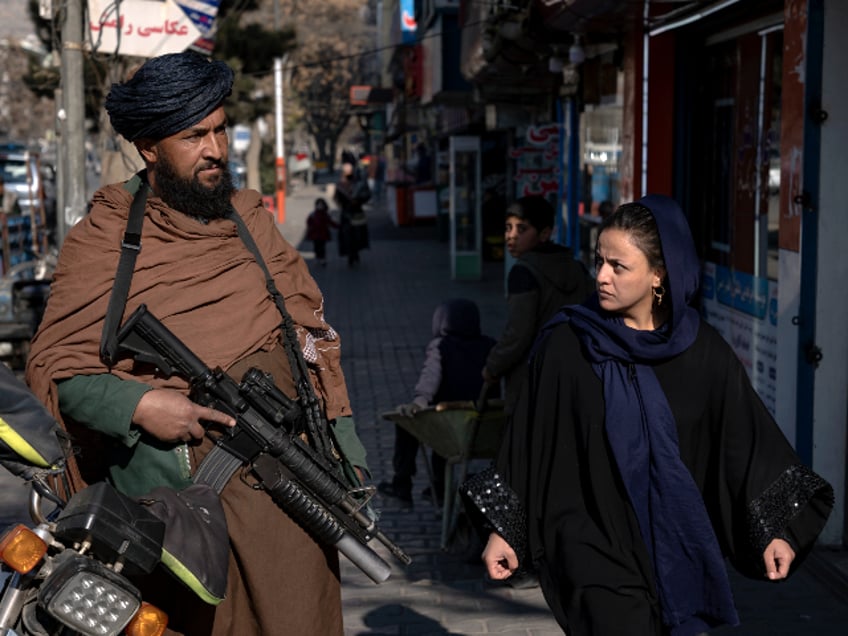 A Taliban fighter stands guard as a woman walks past in Kabul, Afghanistan, Monday, Dec. 26, 2022. Recent Taliban rulings on Afghan women include bans on university education and working for NGOs, sparking protests in major cities. Security in the capital Kabul has intensified in recent days, with more checkpoints, armed vehicles, and Taliban special forces on the streets. Authorities have not given a reason for the tougher security. (AP Photo/Ebrahim Noroozi)