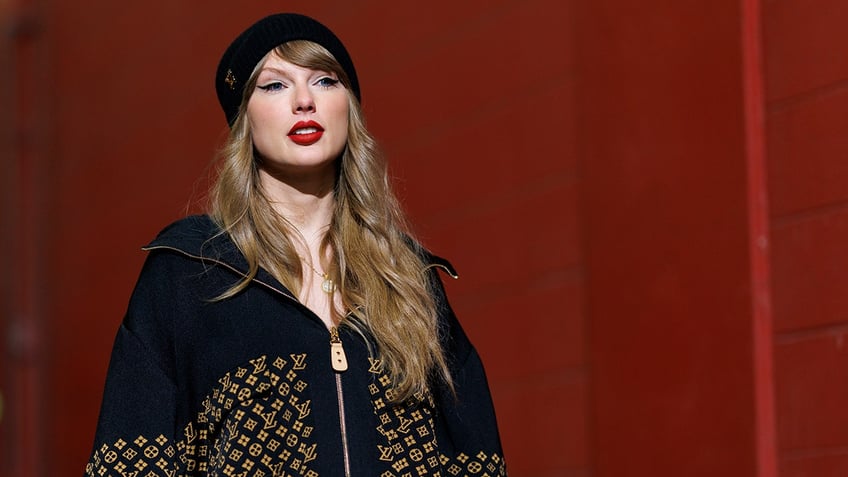 Taylor Swift walks down a hallway wearing a Louis Vuitton jacket and hat 