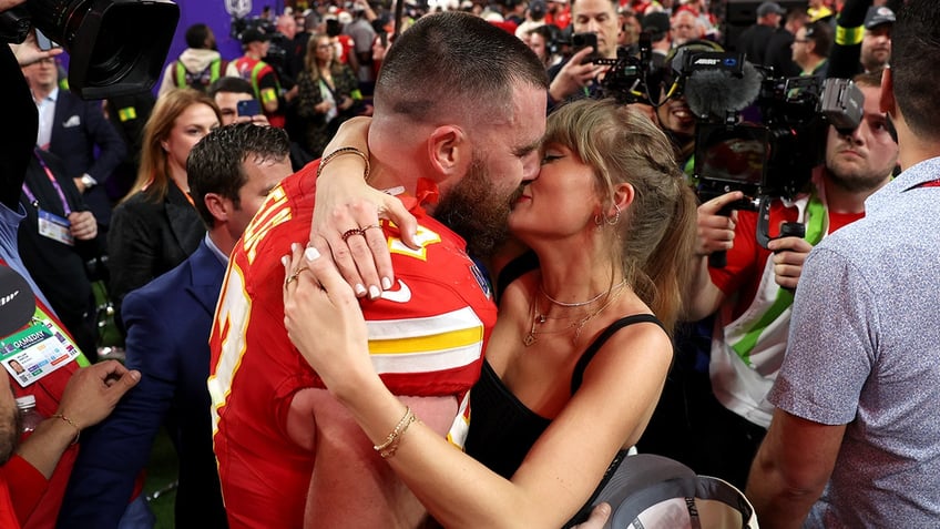 Travis Kelce in a red Kansas City Chiefs jersey kisses Taylor Swift in a black tank top after winning the Super Bowl