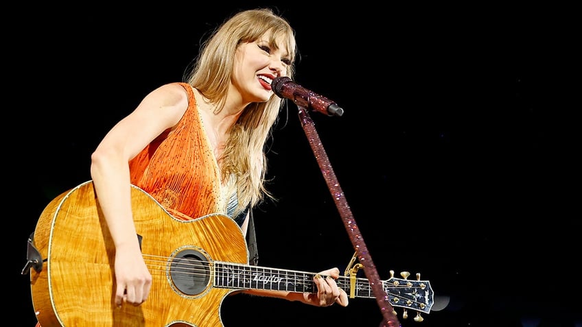 Taylor Swift wearing orange on stage and holding her guitar