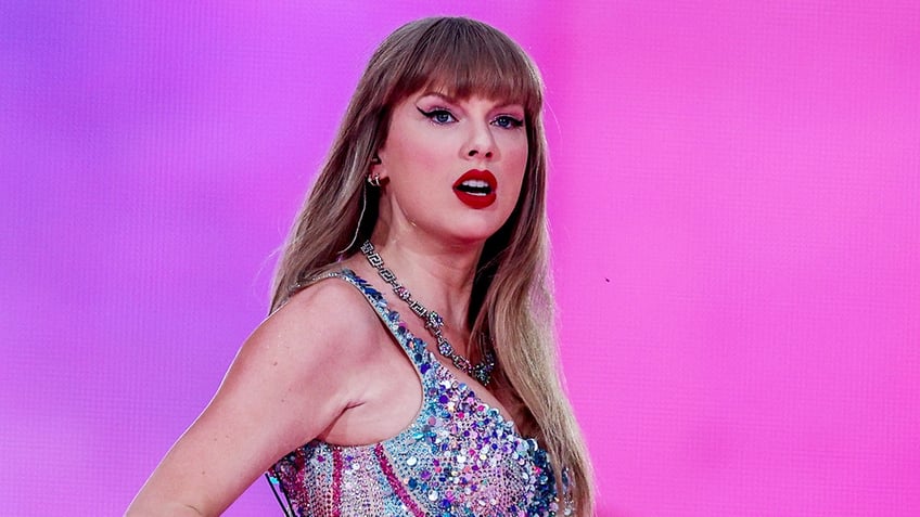 Taylor Swift in a multicolored sparkly bodysuit looks serious as she looks out into the crowd