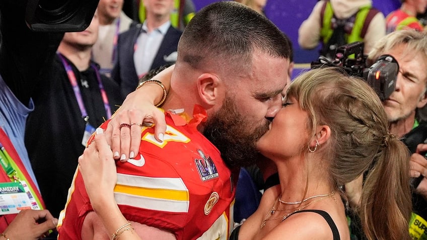 Travis Kelce in his red Chiefs uniform kisses Taylor Swift on the field after winning the Super Bowl