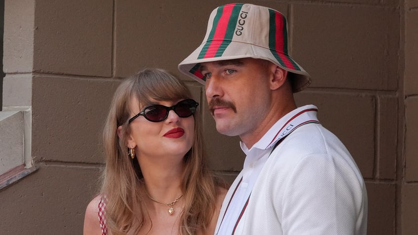 Taylor Swift in black sunglasses looks slightly up and smirks at boyfriend Travis Kelce wearing a Gucci bucket hat at the US OPEN