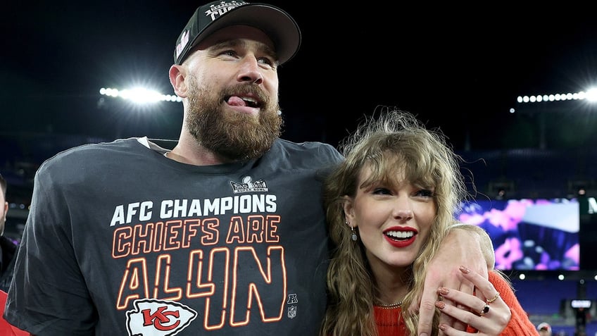 Travis Kelce wraps his arm around Taylor Swift wearing an AFC Champions shirt while Taylor wears a red sweatshirt