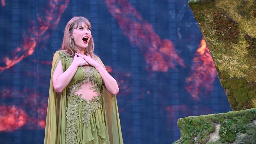 Taylor Swift in a green dress smiles at the crowd during Eras Tour