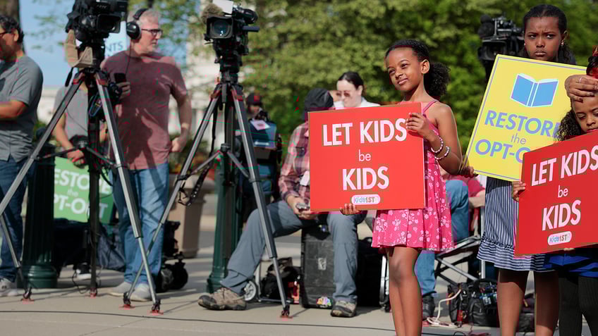 Girl holding 'let kids be kids' sign
