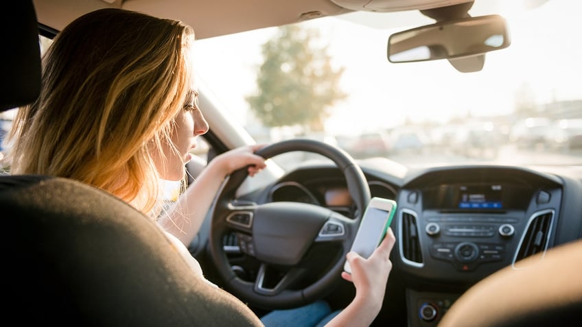 Young woman looks at cell phone in car
