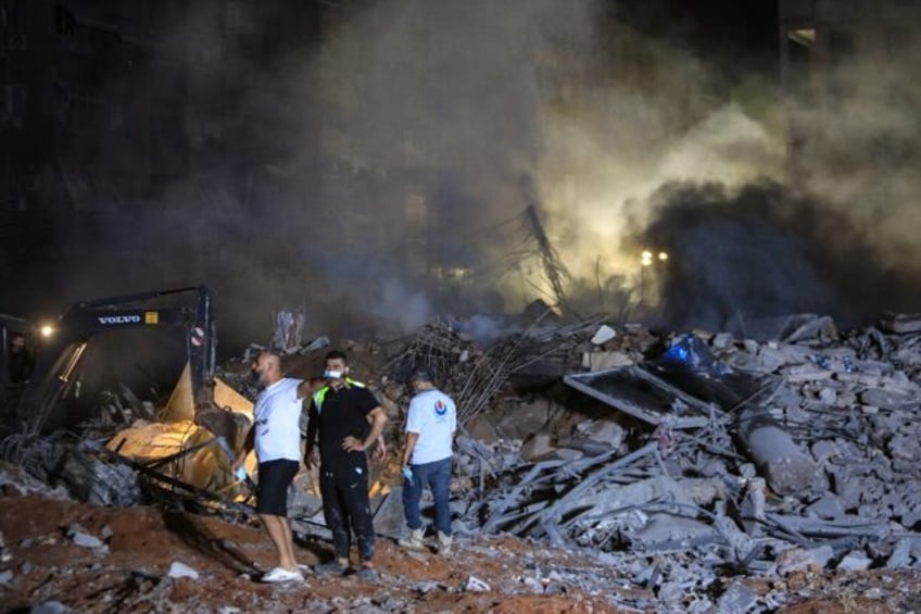 Rescuers stand on the rubble of a builiding destroyed in an Israeli air strike in Haret Hr