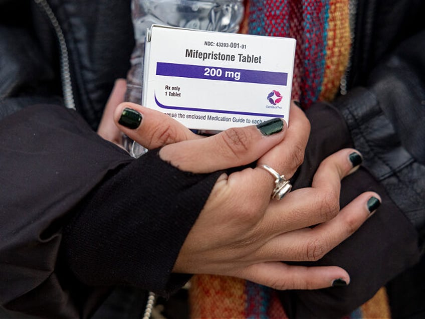 An abortion- rights activist holds a box of mifepristone pills as demonstrators from both