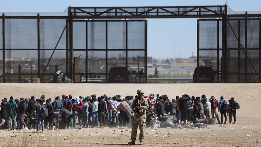 Migrants, border official near the border wall