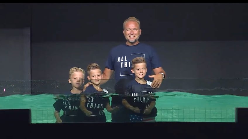 Jeremiah Johnston with his three boys, standing in a pool of green water. Everyone is smiling.