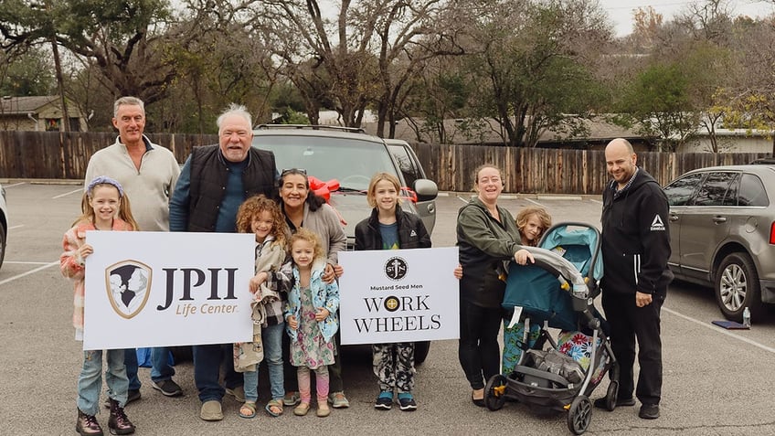 people in front of car holding signs for "Work Wheels" and "JPII Center"
