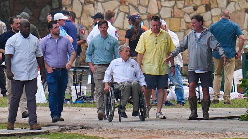 Texas Gov. Greg Abbott, center, tours Camp Mystic along the banks of the Guadalupe River after a flash flood swept through the area Saturday, July 5, 2025, in Hunt, Texas. 