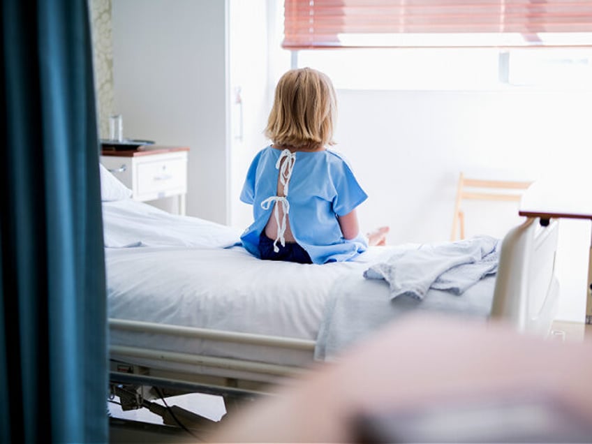Rear view of ill girl sitting on bed. Female child patient is wearing hospital gown. She i