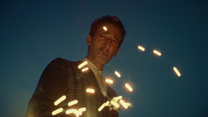 Adrien Brody with sparks flying in front of his face in a scene from "The Brutalist"