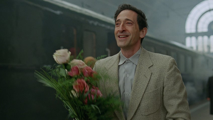 Adrien Brody carrying flowers in a scene from "The Brutalist."