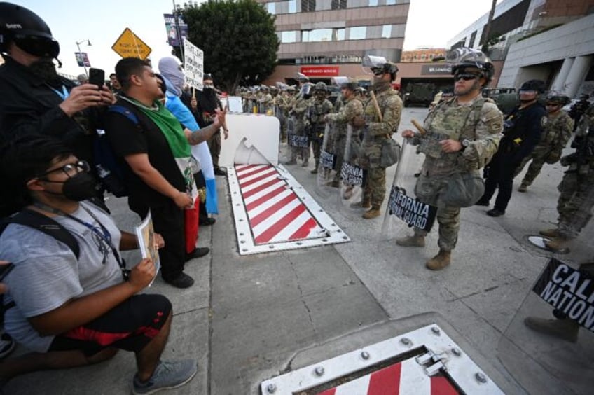 Protestors stand in front California National Guard members at a federal building in Los A