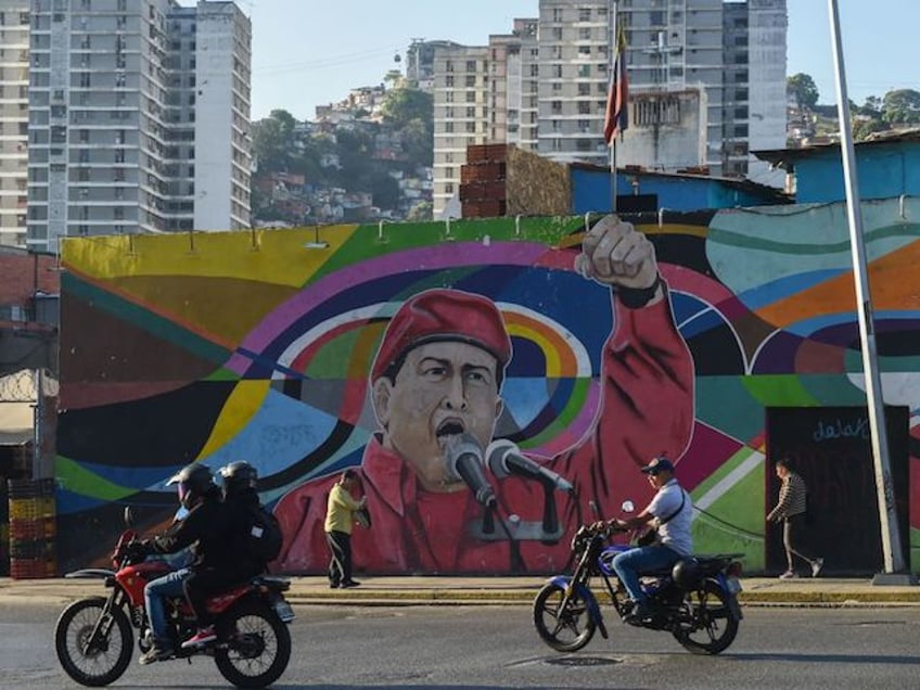 Men on motorcycles ride past a mural depicting Venezuela's late President Hugo Chavez (1954-2013) in Caracas, Venezuela, March 2, 2023. - Massive protests repressed by the military and police, with dozens of deaths. Economic collapse. A failed parallel opposition government. International sanctions. Led by the designated successor Nicolas Maduro, Venezuela has experienced a decade of conflict since the death of the socialist president Hugo Chavez on March 5, 2013. (Photo by Miguel ZAMBRANO / AFP) (Photo by MIGUEL ZAMBRANO/AFP via Getty Images)
