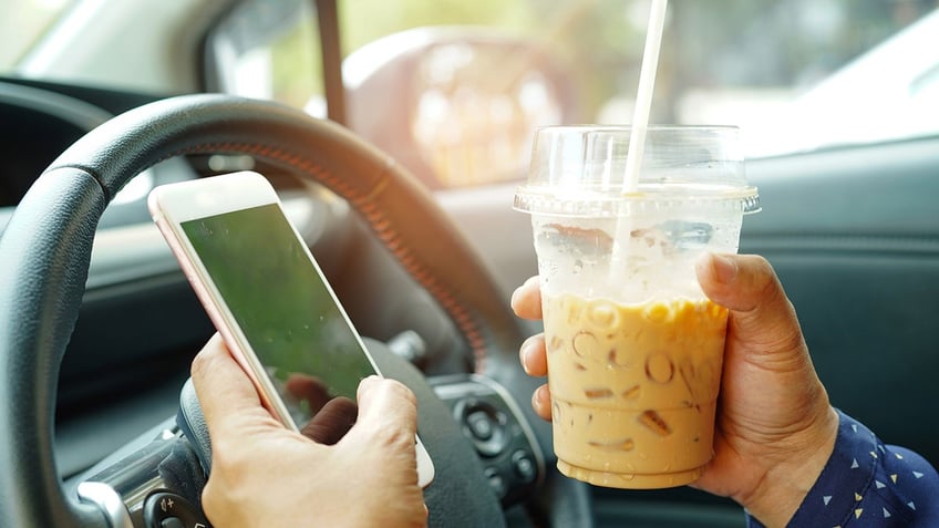 Driver holding ice coffee and phone in car