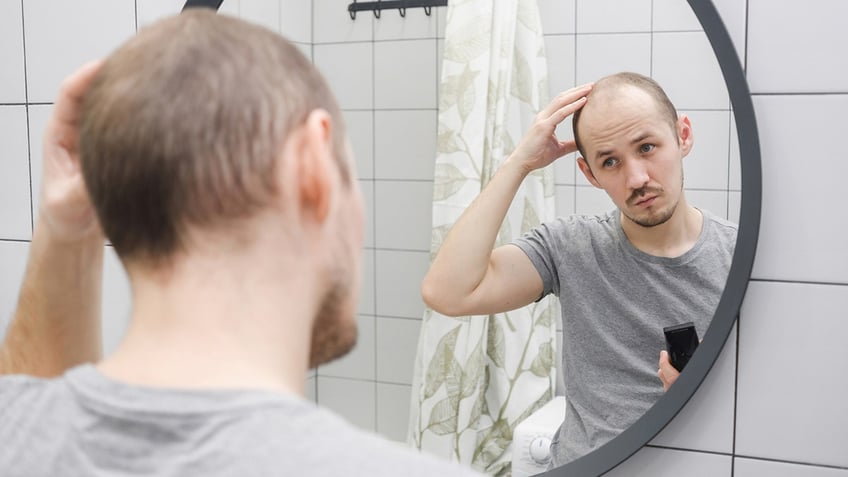 A man looking at his hair in the mirror in the bathroom