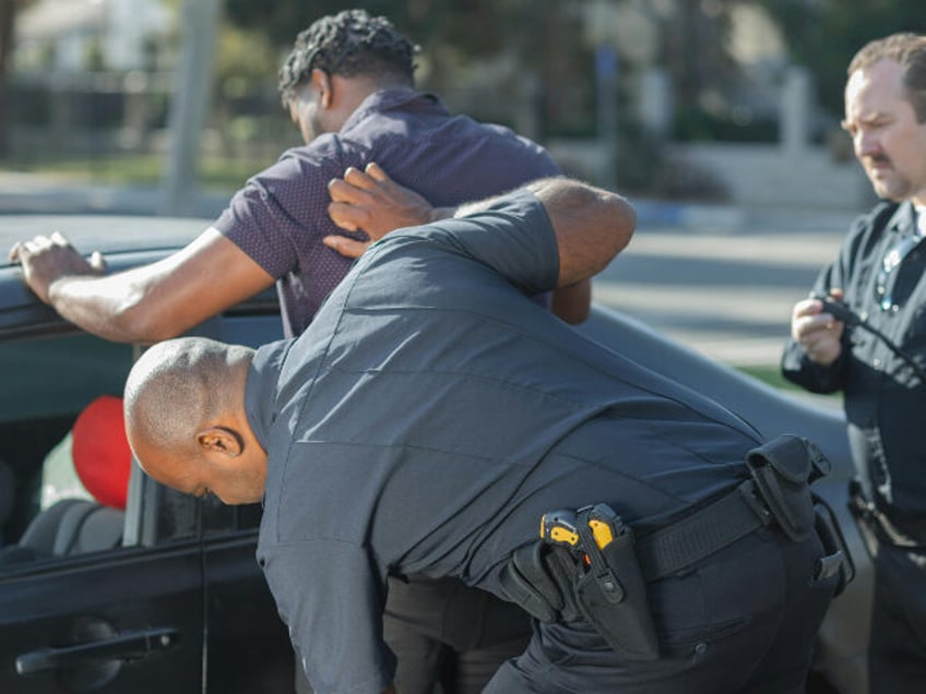 man in gray t-shirt being searched by two police officers