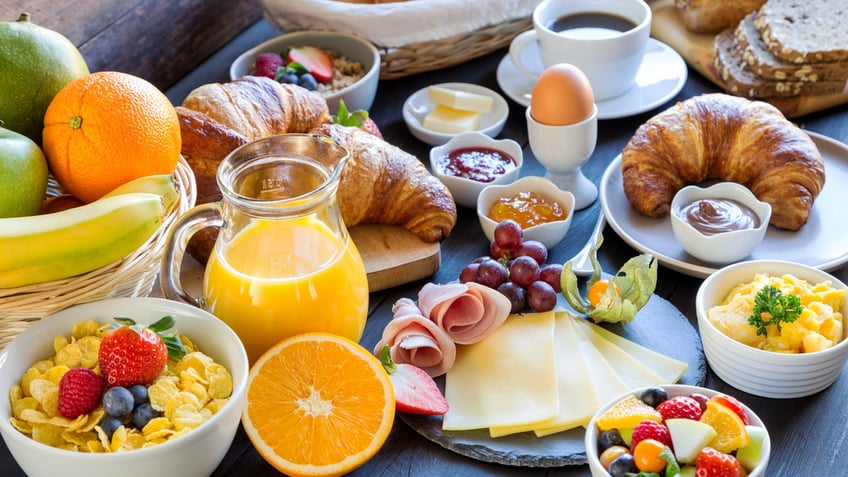 breakfast spread including juice, fruits, meat and cheese, croissants and eggs.