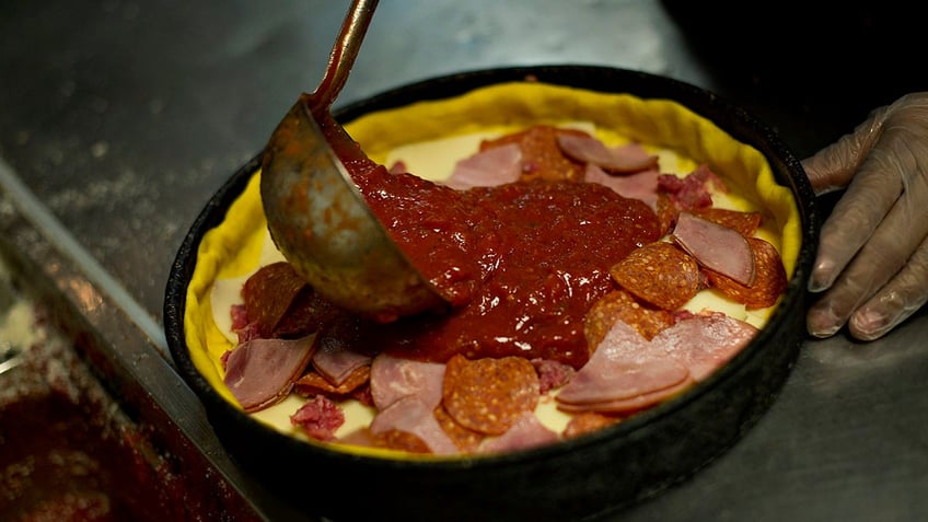 A person making a deep dish pizza, which involves putting sauce on top of toppings.