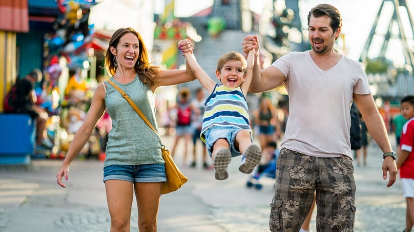 Two parents swinging child in the air at amusement park