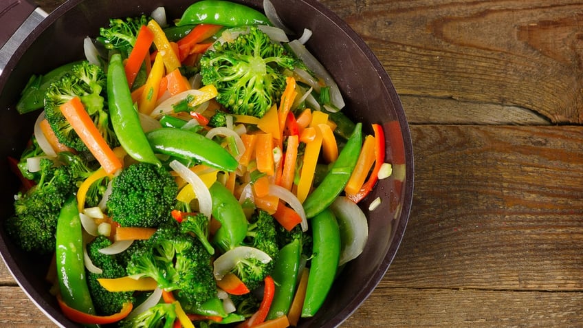 A rainbow veggie stir-fry meal is seen in a pan on a wooden surface.