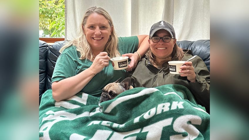 Two women eating chowder while wrapped in a New York Jets blanket.